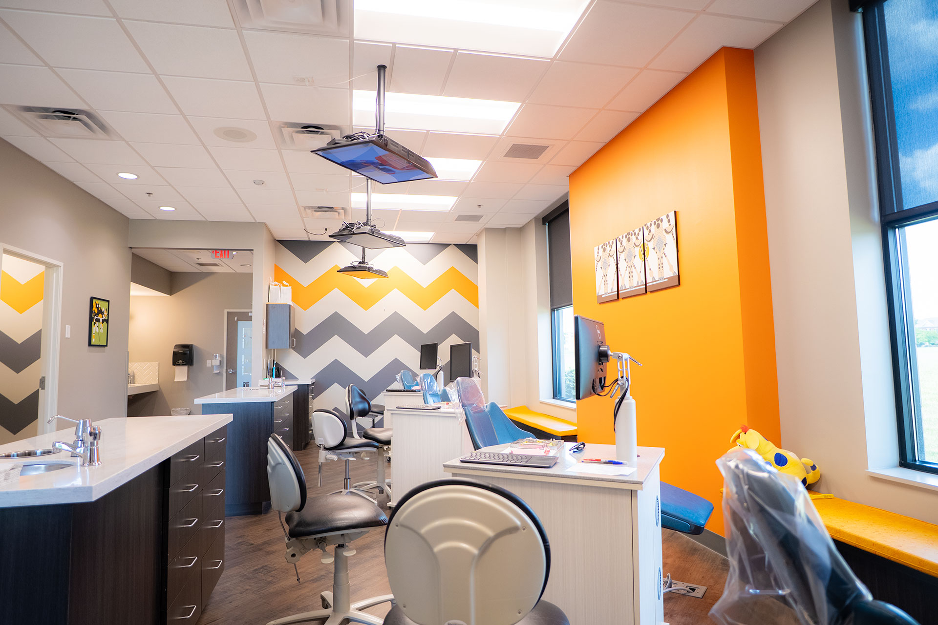 vds-office-7jpg Bright pediatric dental room with colorful chevron walls and treatment chairs.